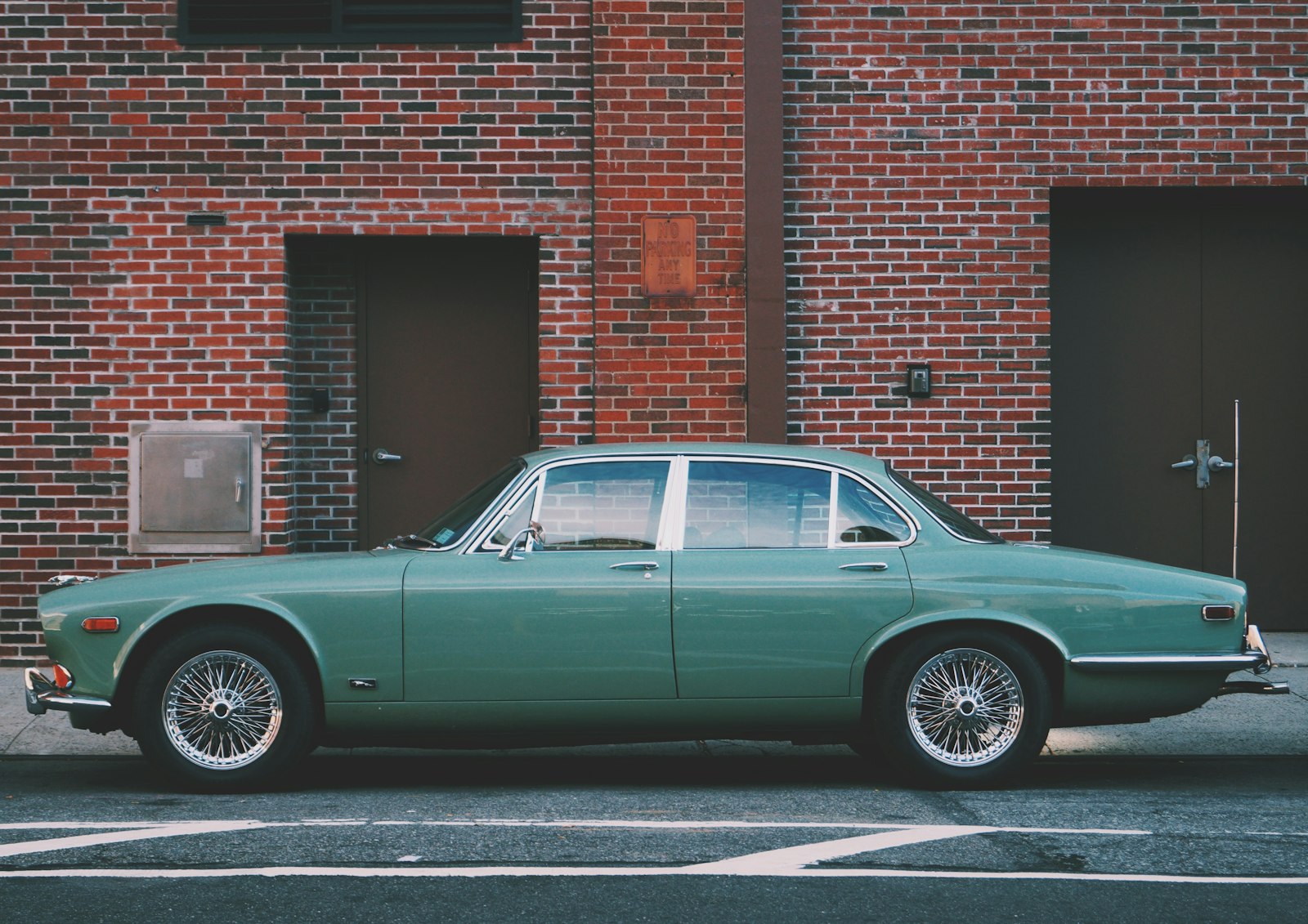 A teal classic saloon car parked alongside a red brick wall